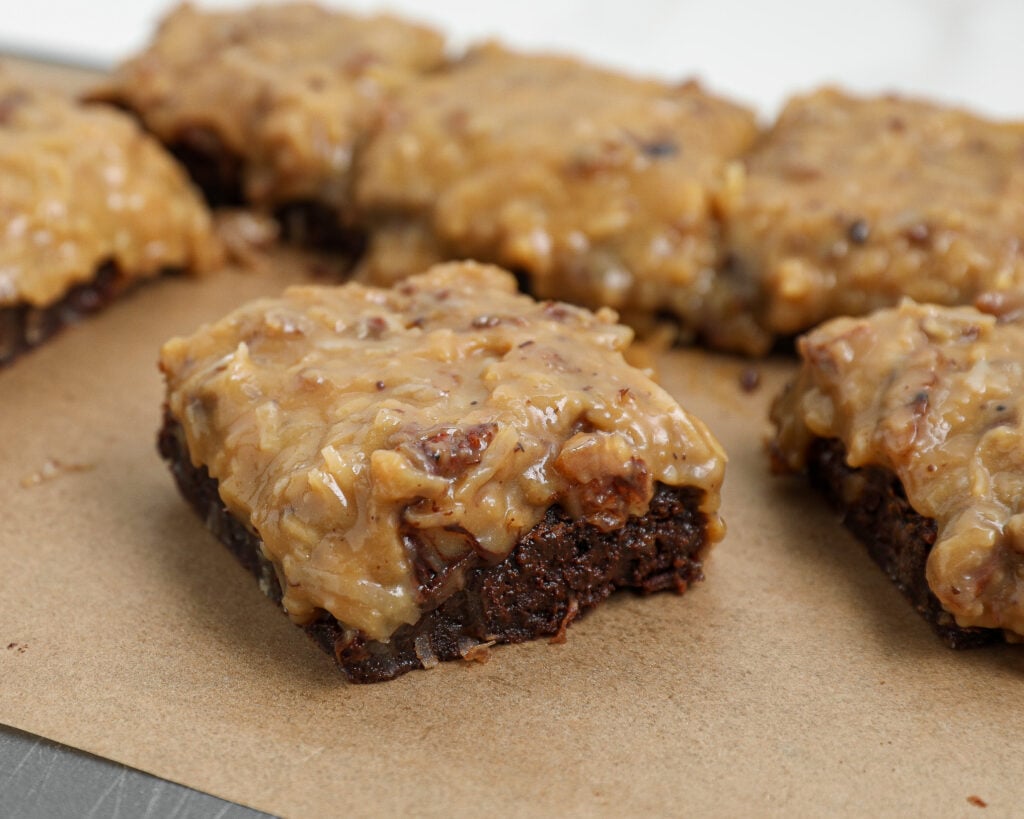 German chocolate brownies topped with homemade coconut pecan frosting on parchment paper.