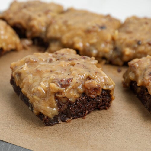 German chocolate brownies topped with homemade coconut pecan frosting on parchment paper.