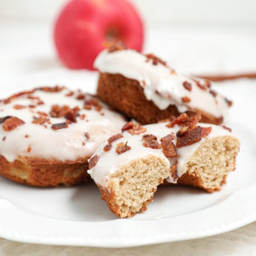 Baked Apple Bacon Donuts topped with vanilla glaze and crispy bacon on a white plate.