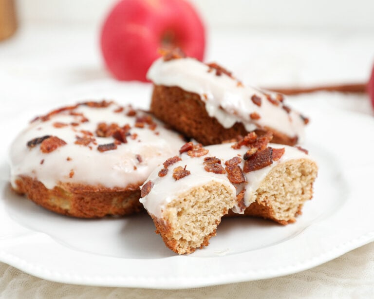 Baked Apple Bacon Donuts topped with vanilla glaze and crispy bacon on a white plate.