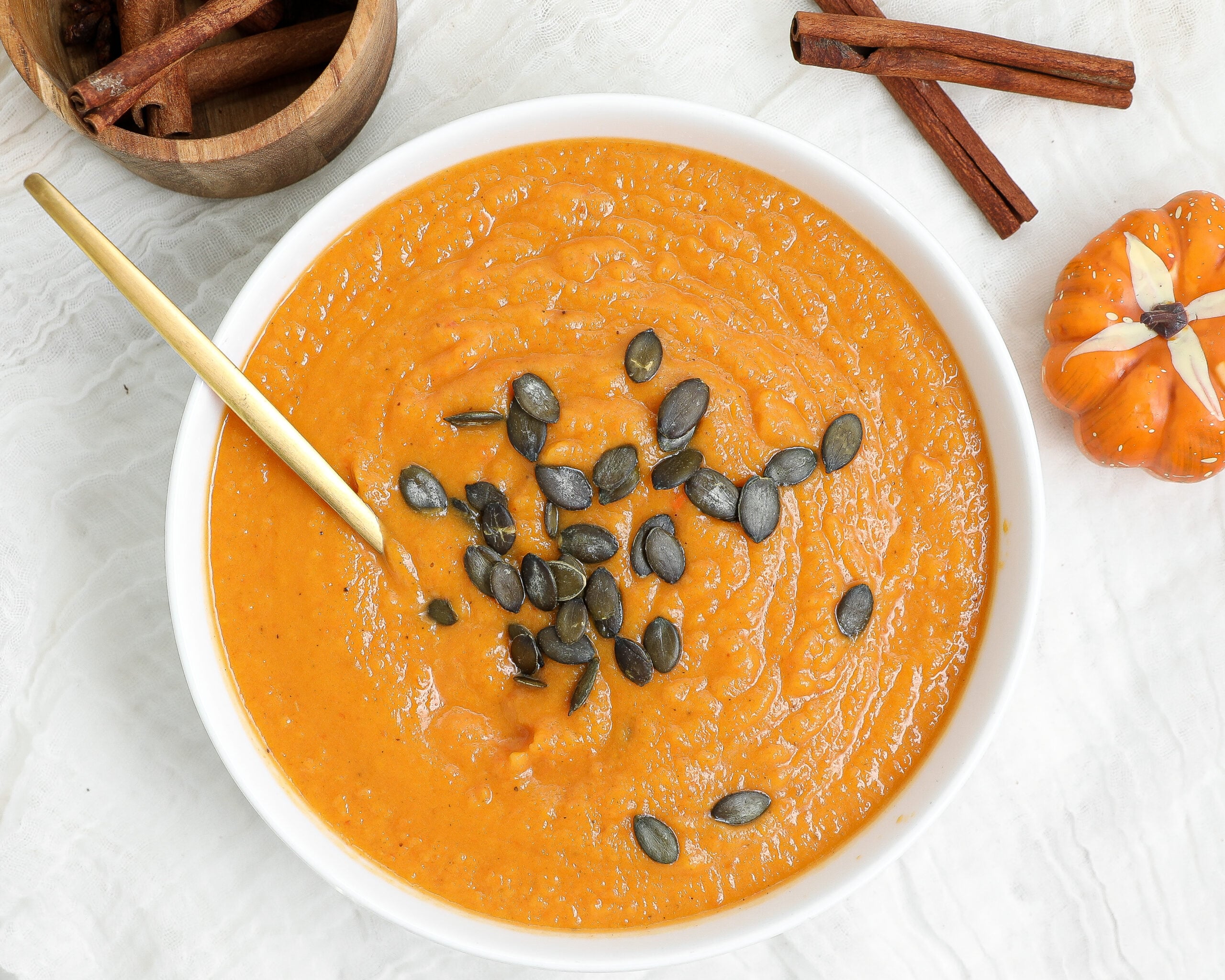 Creamy roasted butternut squash soup topped with pumpkin seeds in a white bowl with a gold spoon.