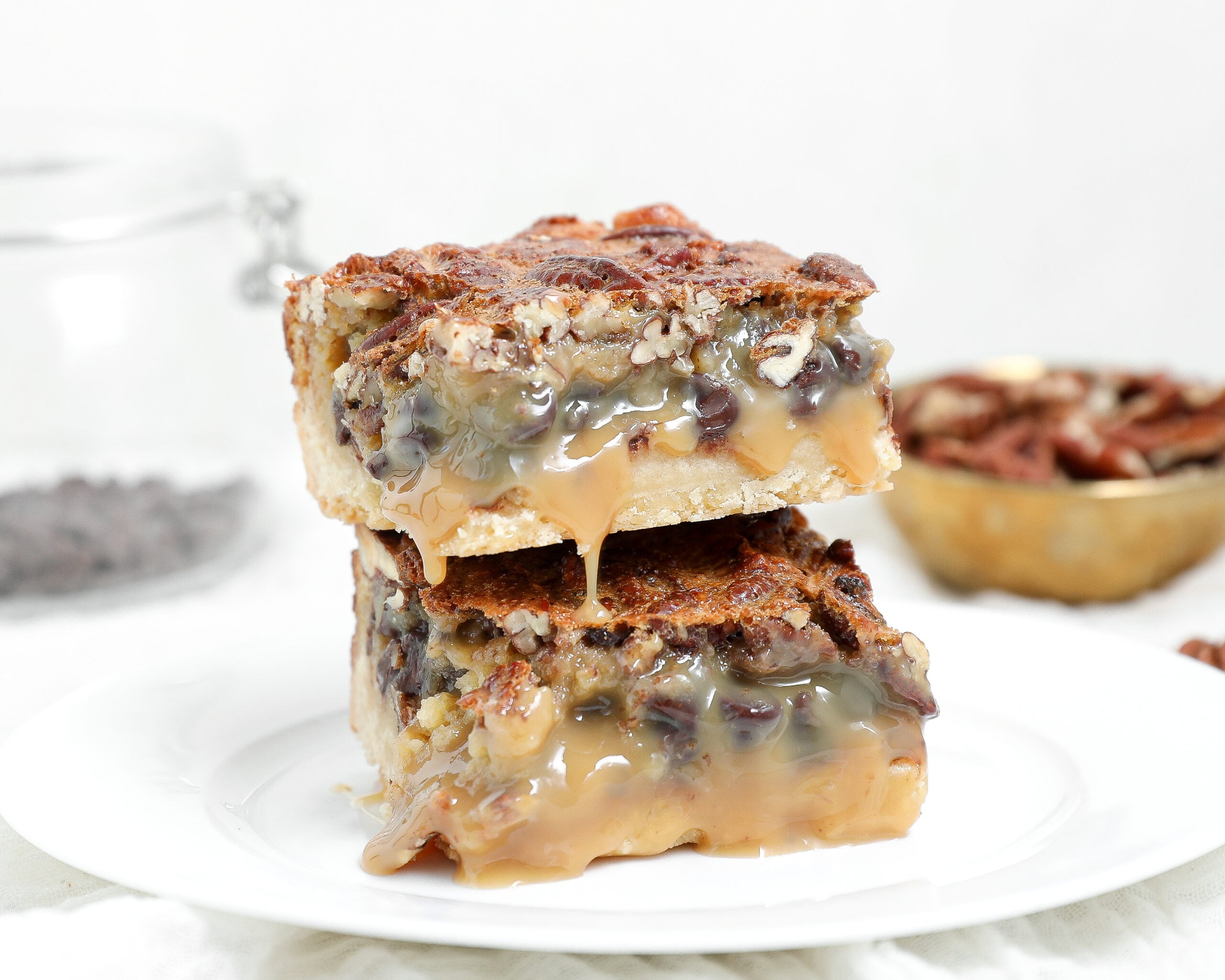 Two stacked chocolate pecan pie bars with a buttery shortbread crust, pecan topping, and gooey caramel-like filling dripping down the sides.