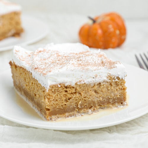 Pumpkin Tres Leches Cake topped with whipped cream and pumpkin spice on a white plate