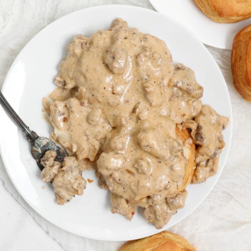 Sausage Gravy and Biscuits served over flaky homemade buttermilk biscuits in a white bowl with fresh cracked black pepper.