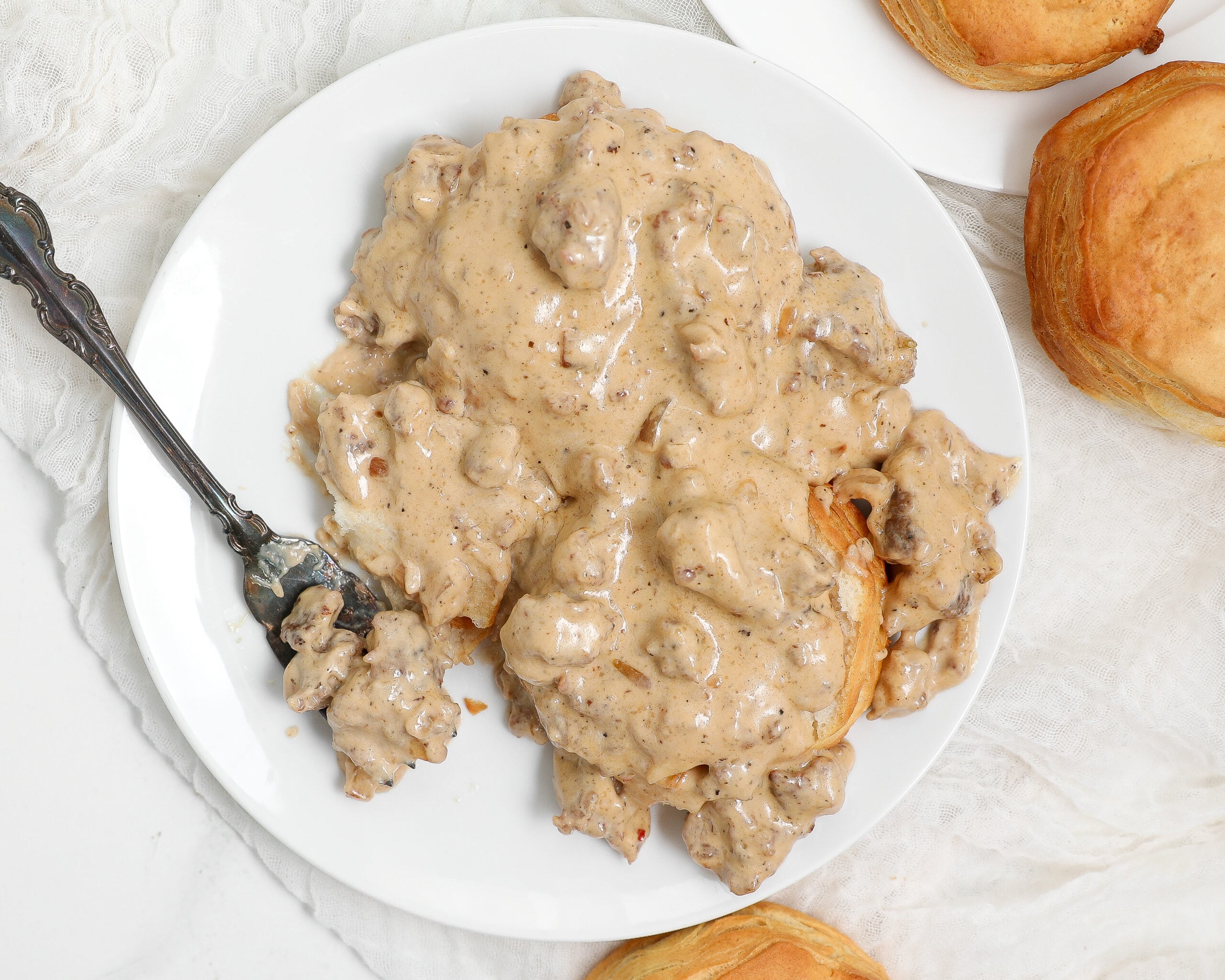 Sausage Gravy and Biscuits served over flaky homemade buttermilk biscuits in a white bowl with fresh cracked black pepper.