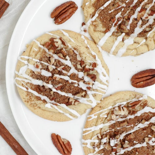 Coffee Cake Cookies topped with cinnamon pecan crumble and drizzled with sweet vanilla glaze on a white plate.