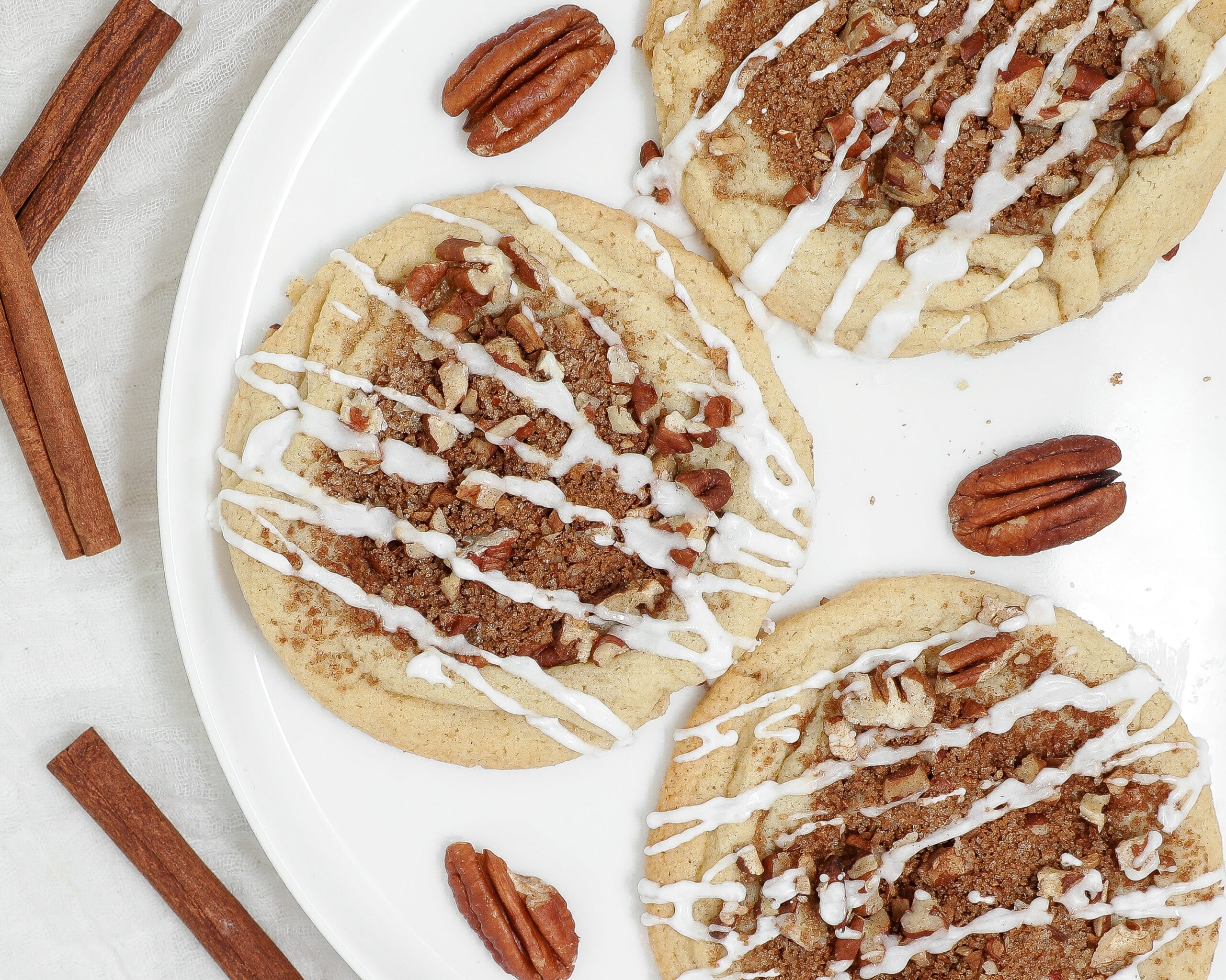 Coffee Cake Cookies topped with cinnamon pecan crumble and drizzled with sweet vanilla glaze on a white plate.