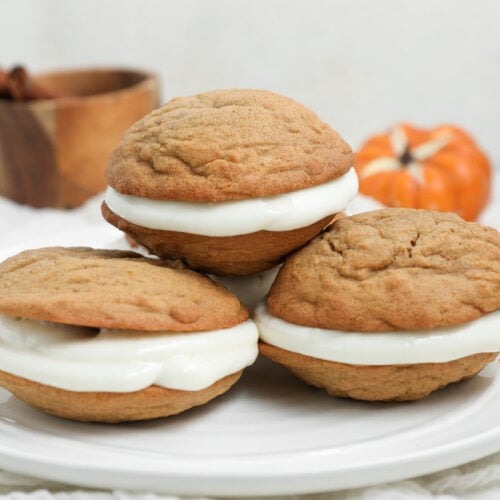 Pumpkin whoopie pies filled with cream cheese frosting and stacked on a white plate.