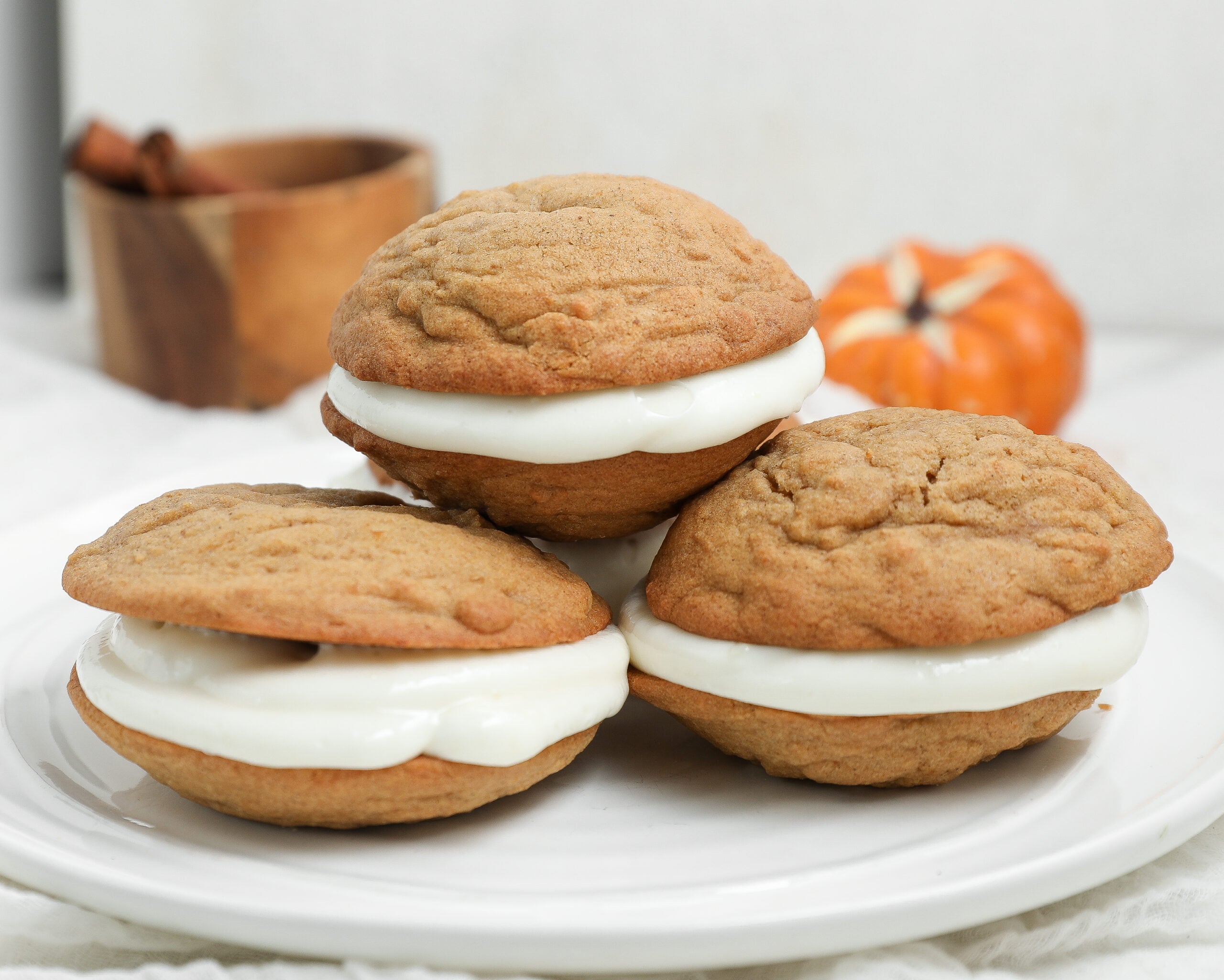 Pumpkin whoopie pies filled with cream cheese frosting and stacked on a white plate.