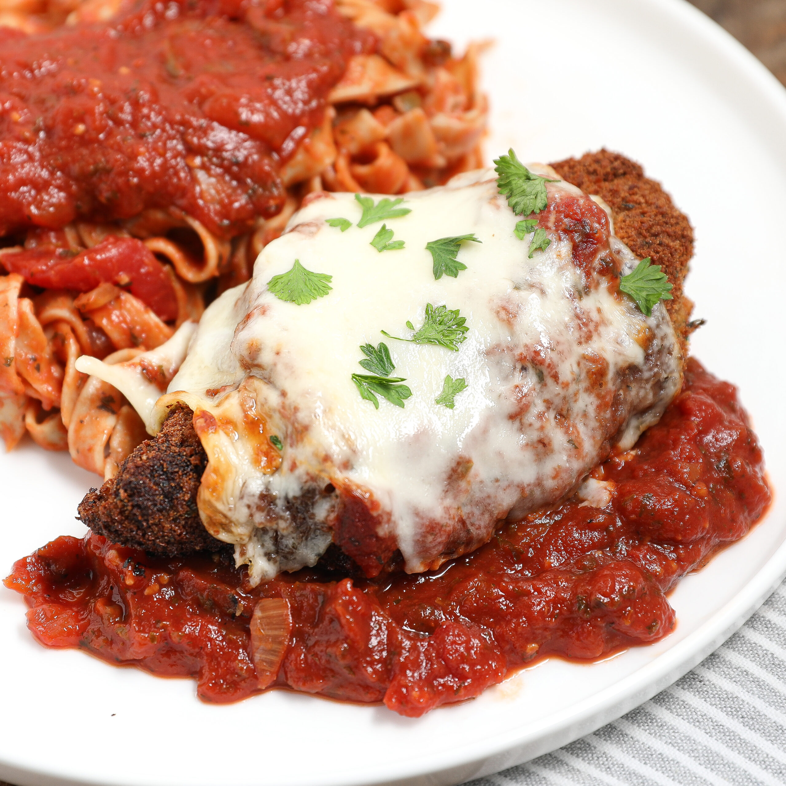 A plate of Chicken Parmesan features breaded chicken topped with melted cheese and parsley, served over tomato sauce, alongside pasta in red sauce.