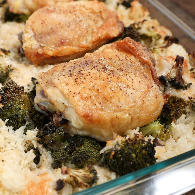 A glass baking dish filled with Parmesan Chicken Broccoli Rice Casserole, featuring golden brown chicken thighs resting atop a bed of cooked rice and roasted broccoli florets.