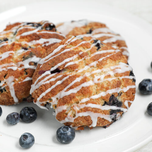 Flaky homemade blueberry biscuits topped with cinnamon glaze and served with fresh blueberries