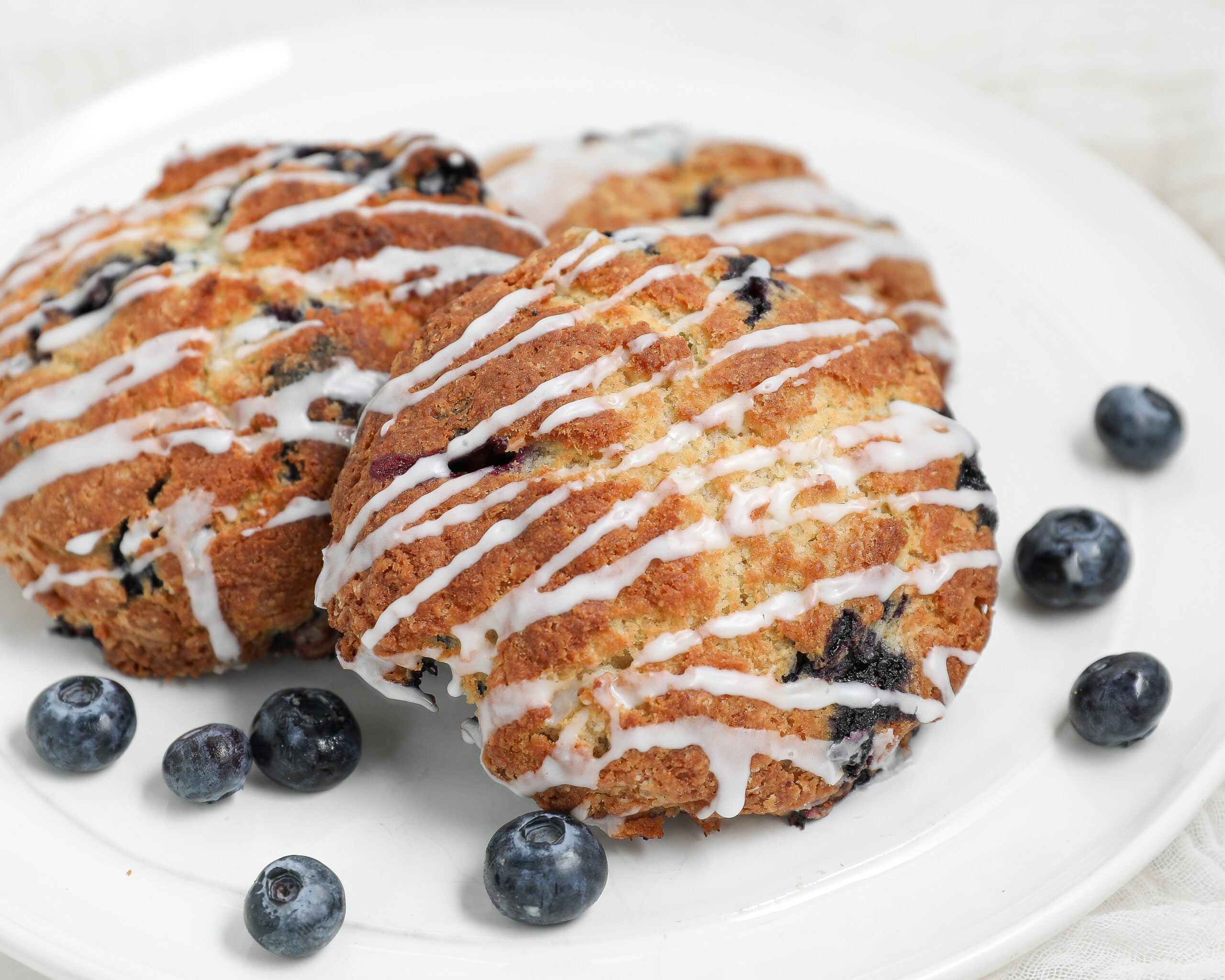 Flaky homemade blueberry biscuits topped with cinnamon glaze and served with fresh blueberries