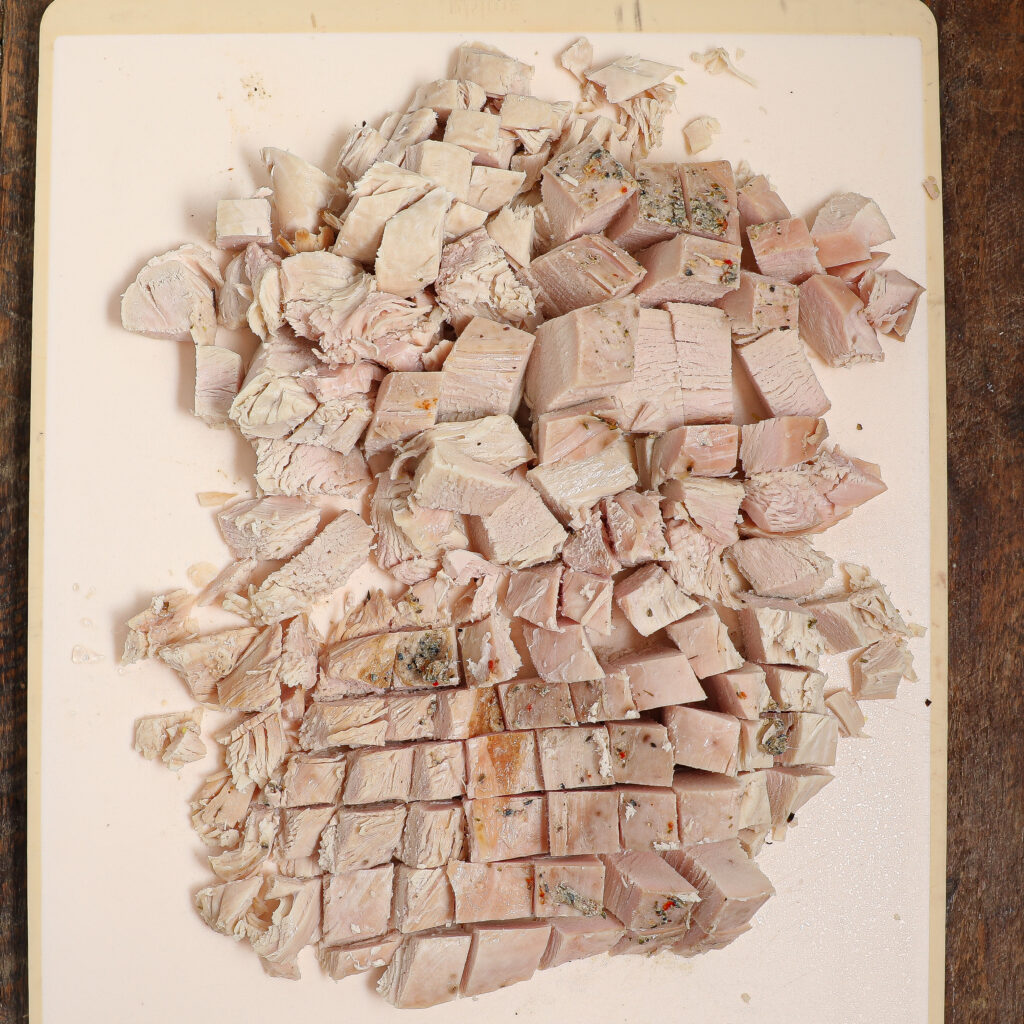 Diced pieces of cooked chicken breast, perfect for Turkey Pot Pie, are arranged on a white cutting board and viewed from above, with some seasoning visible on the chicken.