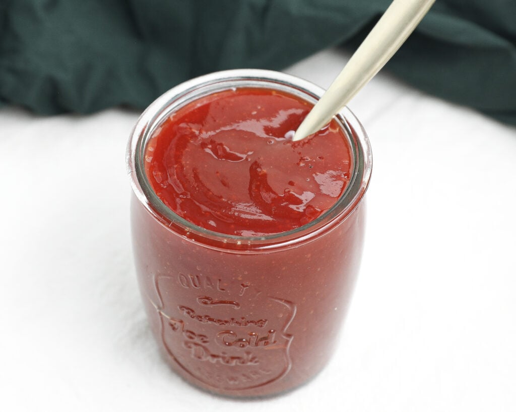 Homemade sweet BBQ sauce in a glass jar with a spoon