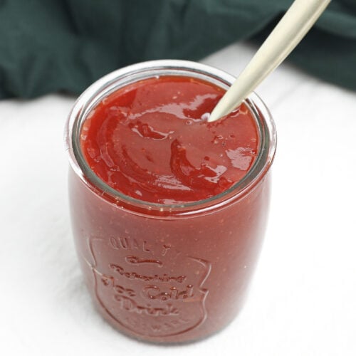Homemade sweet BBQ sauce in a glass jar with a spoon