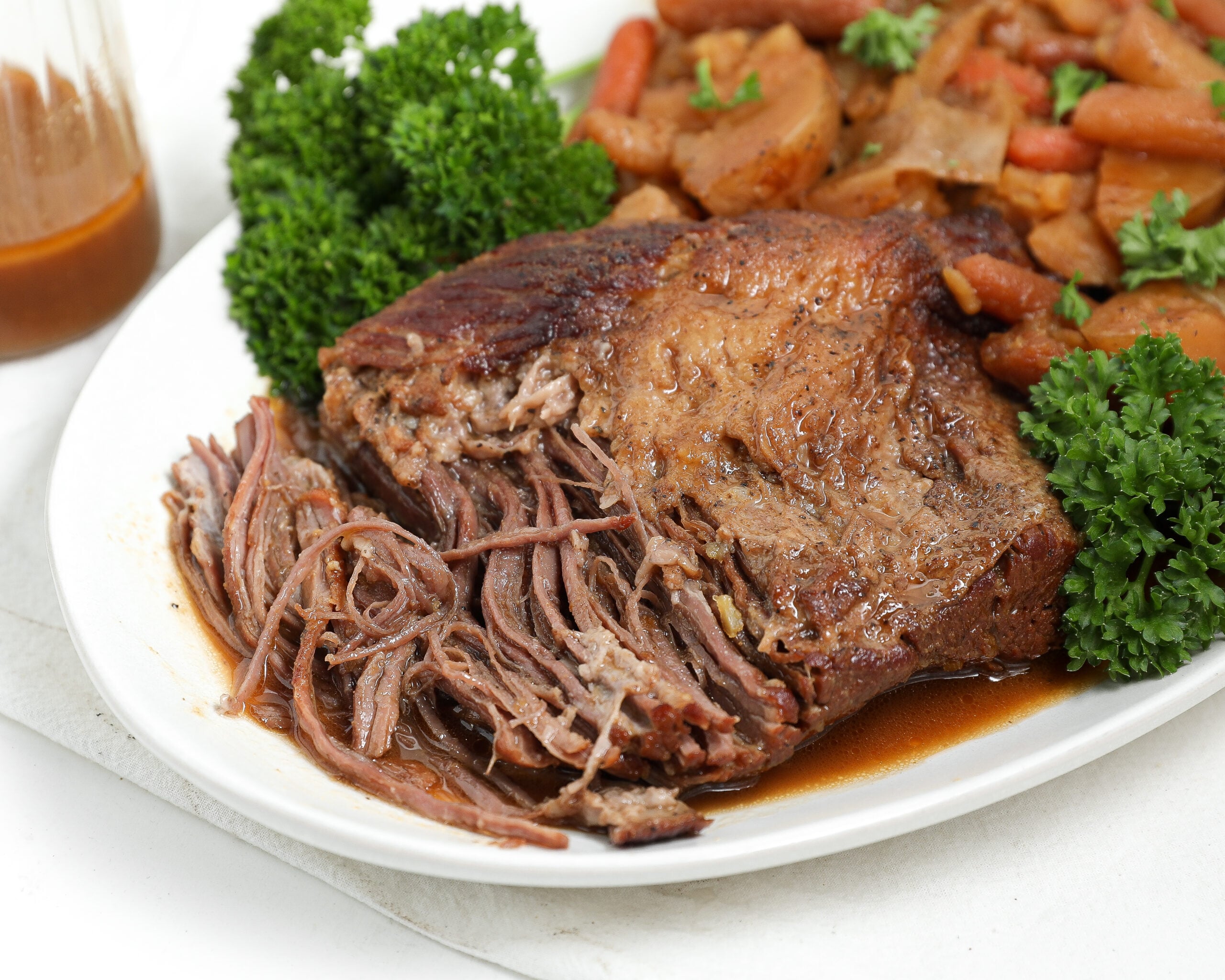 Close-up of oven braised brisket on a plate with gravy, carrots, potatoes, and parsley.