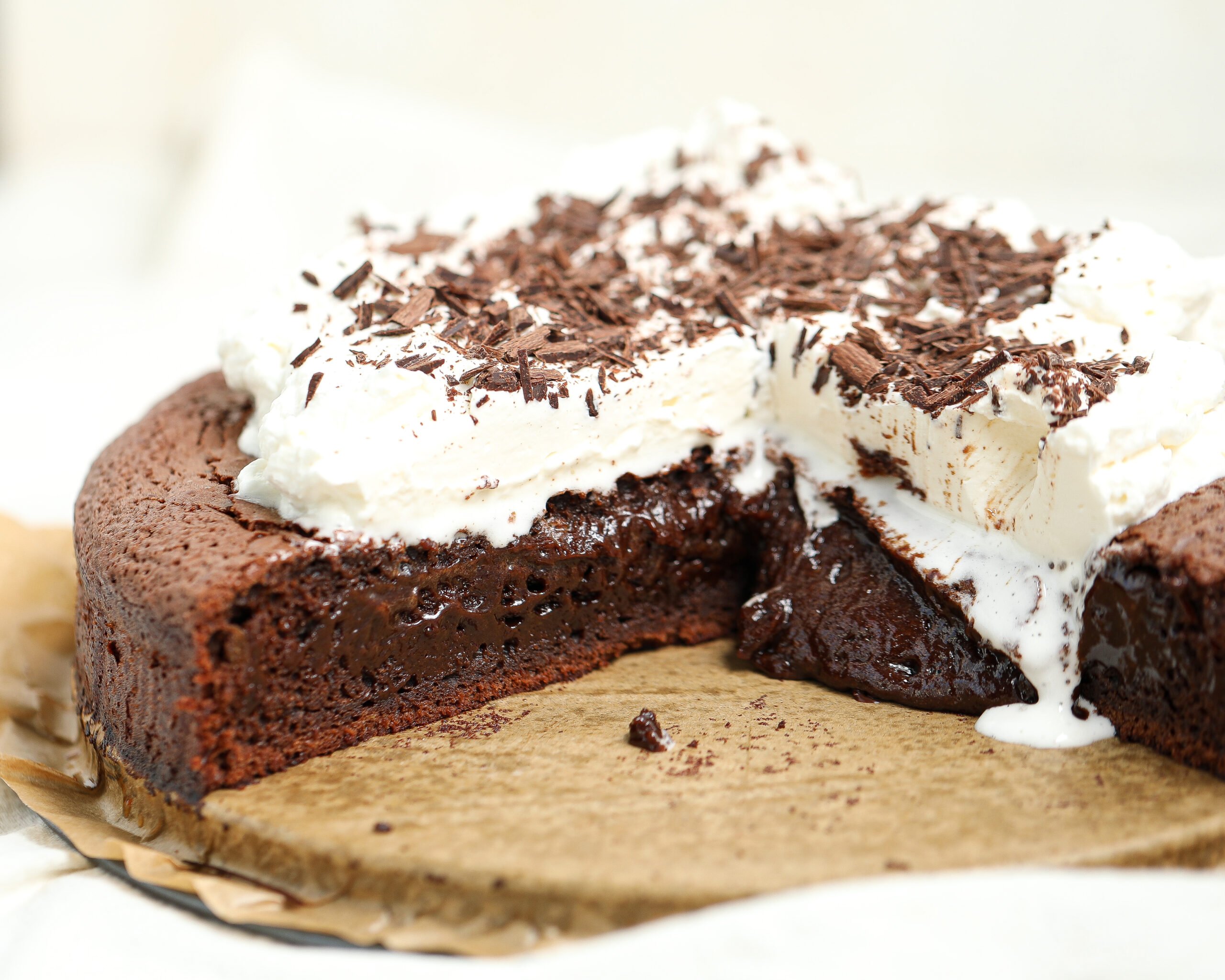 A rich French molten lava cake with a soft, fudgy center oozing onto the parchment-lined board, topped with a thick layer of whipped cream and dark chocolate shavings.