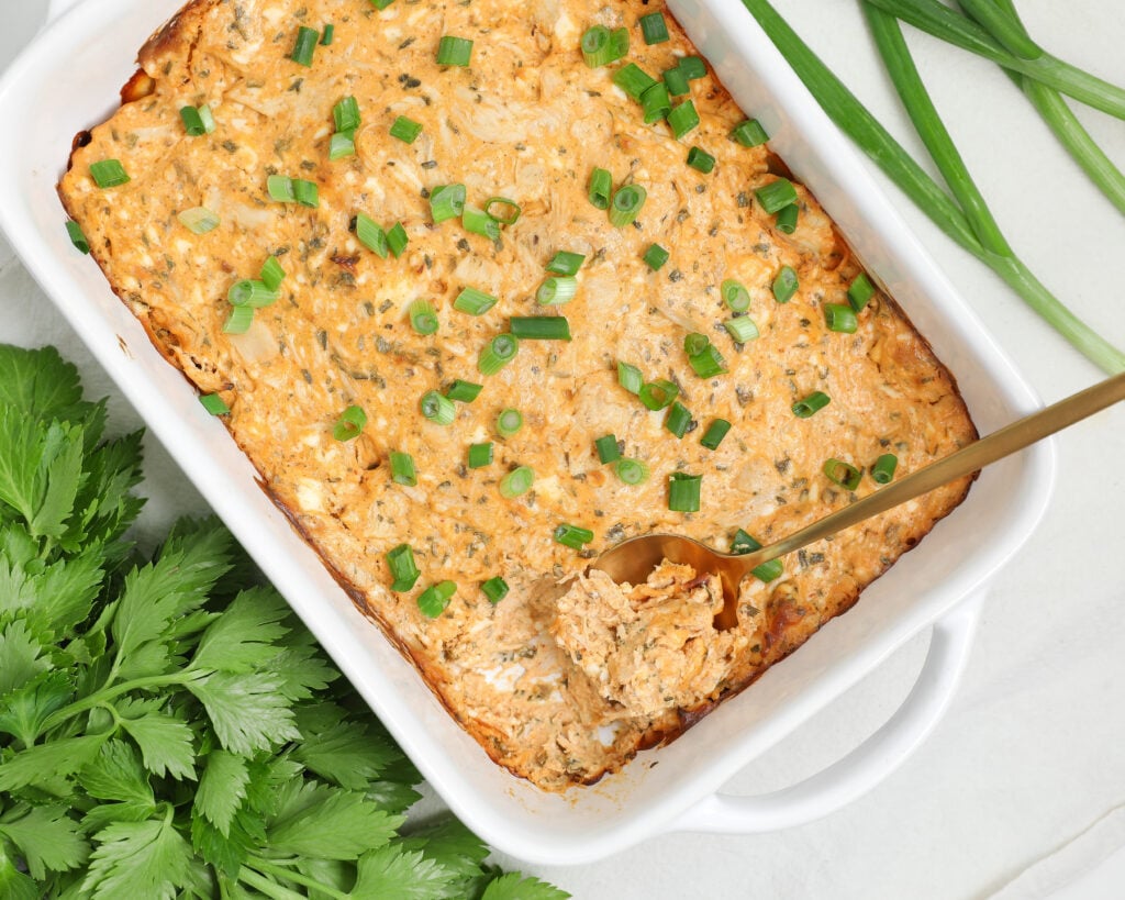 Creamy buffalo chicken dip baked in a white dish and topped with chopped green onions, served hot and ready for dipping.