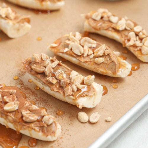 banana slices with peanut butter chopped peanuts honey drizzle and cinnamon on a baking sheet