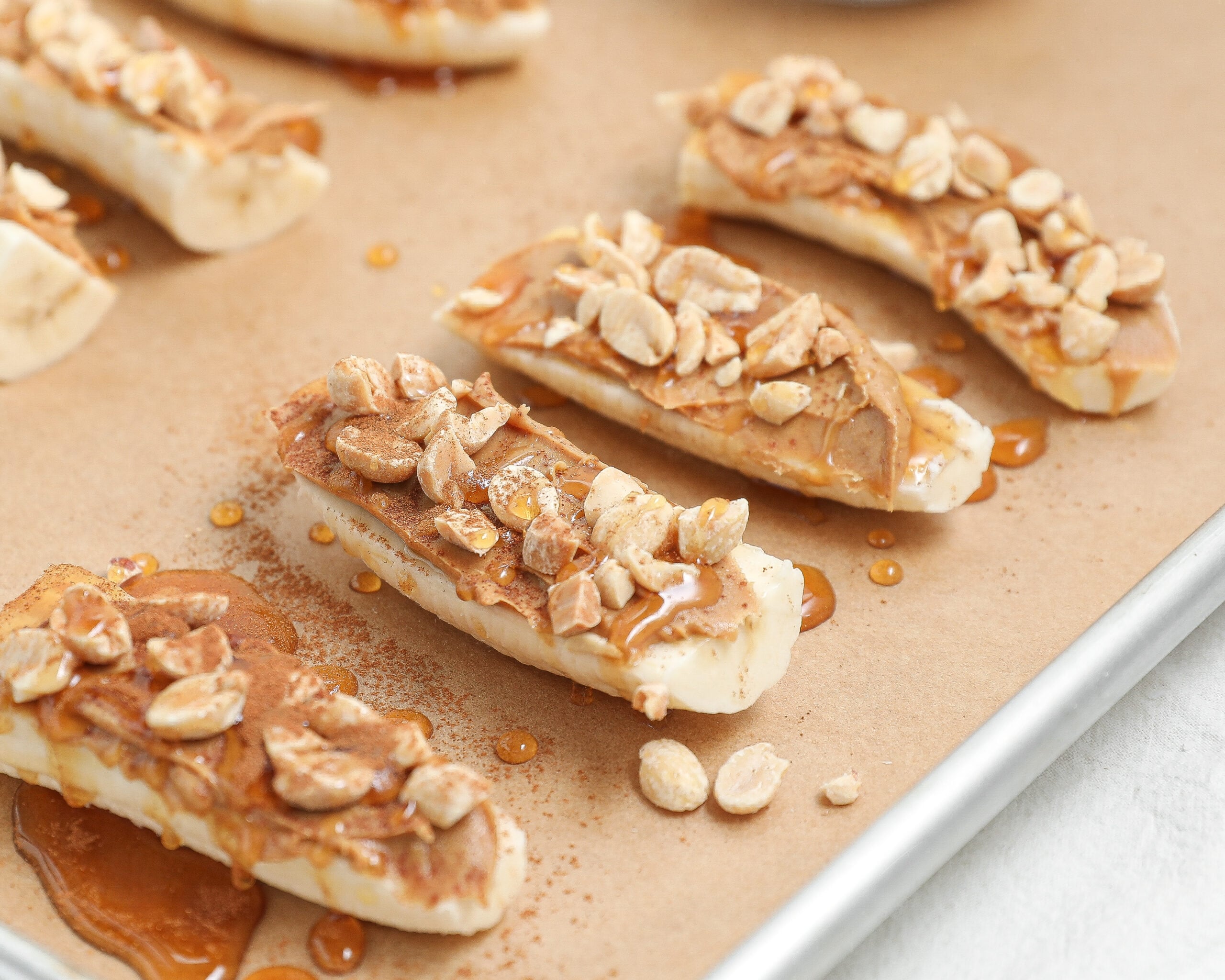banana slices with peanut butter chopped peanuts honey drizzle and cinnamon on a baking sheet