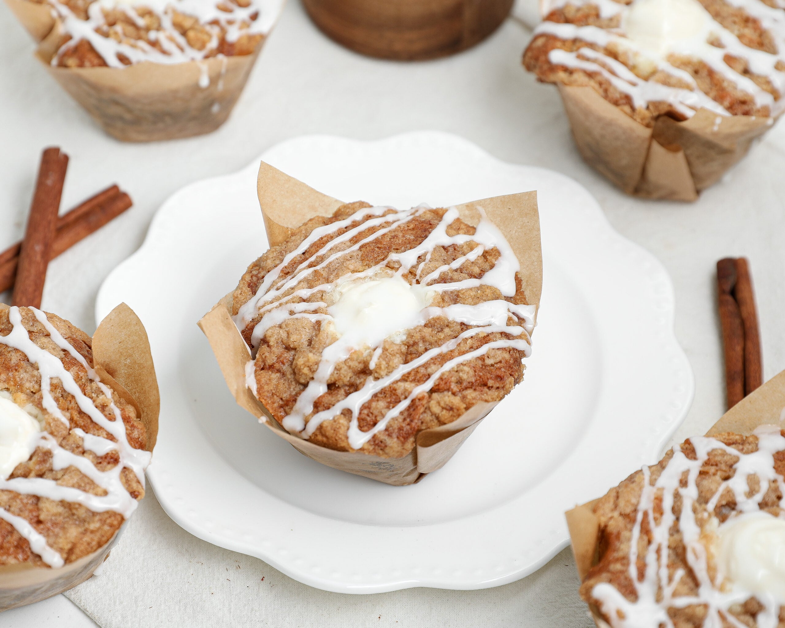 Banana bread coffee cake muffins with cinnamon streusel and vanilla glaze in parchment muffin liners on a white plate.