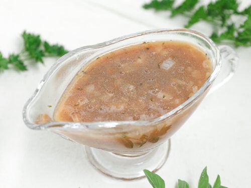 Homemade brown onion gravy with herbs and small onion pieces in a clear glass gravy boat