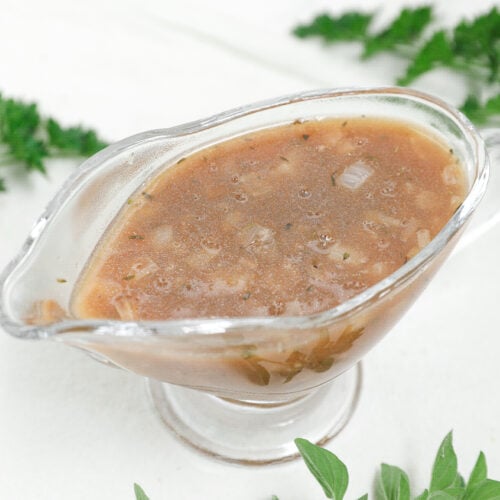 Homemade brown onion gravy with herbs and small onion pieces in a clear glass gravy boat
