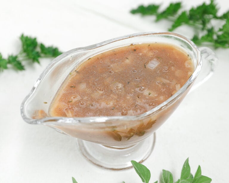 Homemade brown onion gravy with herbs and small onion pieces in a clear glass gravy boat