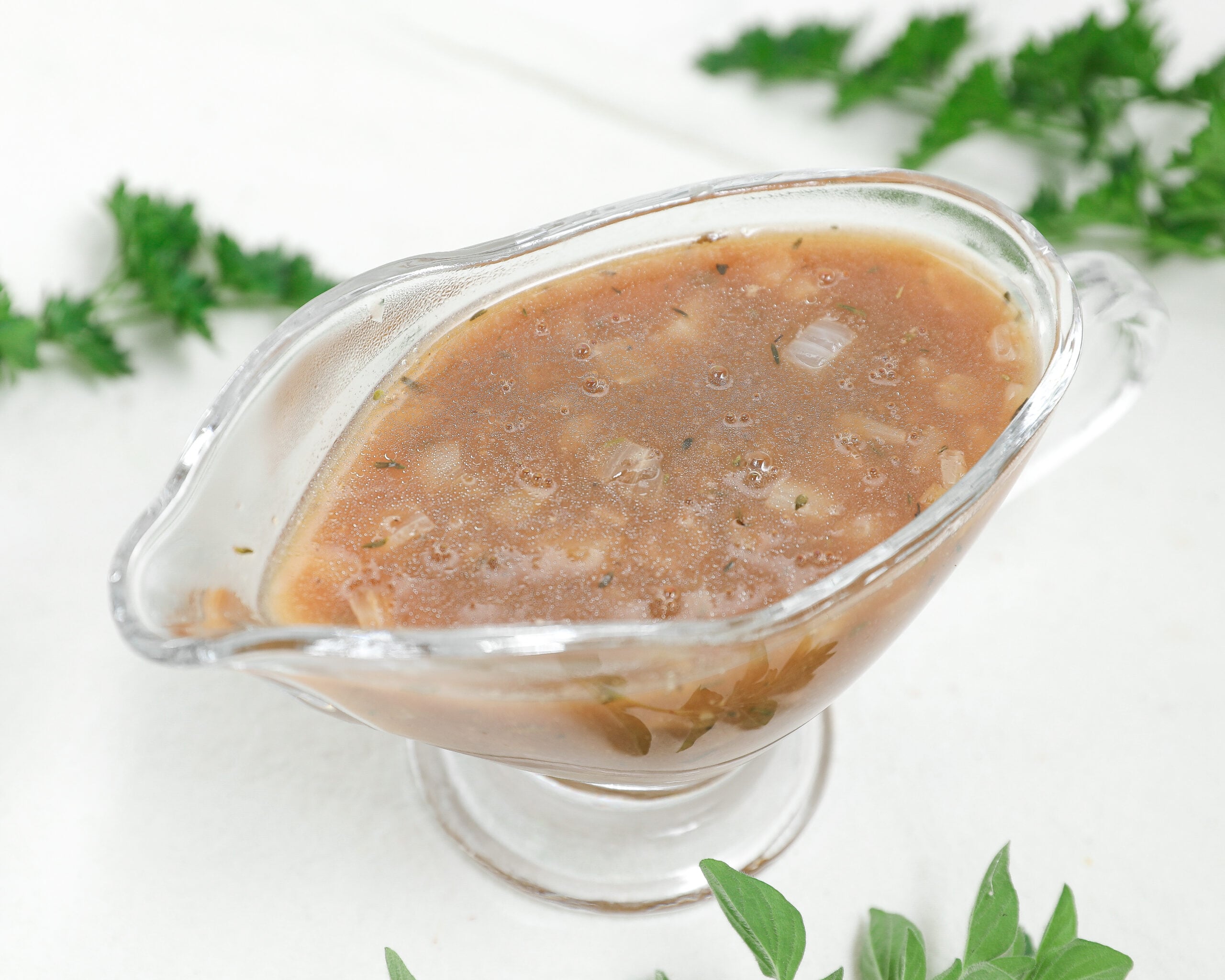 Homemade brown onion gravy with herbs and small onion pieces in a clear glass gravy boat