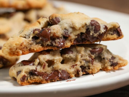 Close-up of soft chocolate chip cookies stacked on a white plate with melted chocolate chips and golden edges.