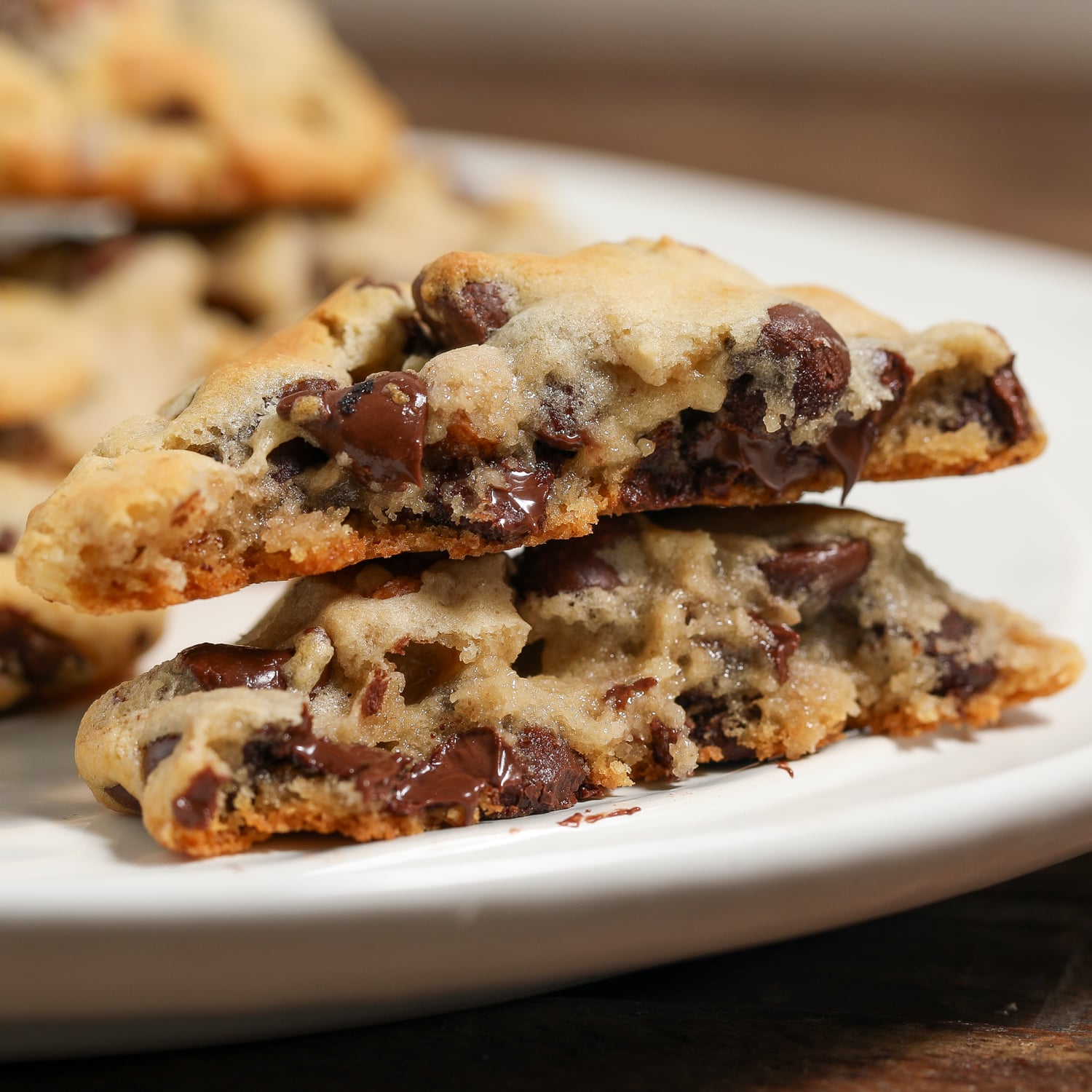 Close-up of soft chocolate chip cookies stacked on a white plate with melted chocolate chips and golden edges.