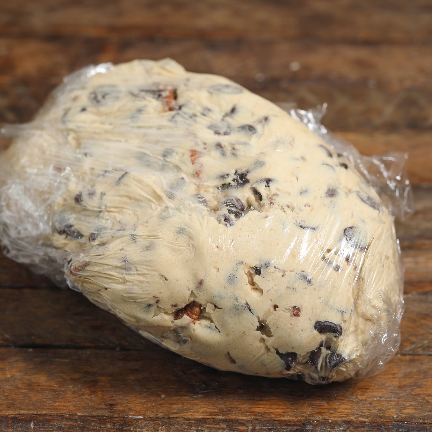 Chilled chocolate chip cookie dough wrapped in plastic wrap on a wooden surface after resting for 24 hours.