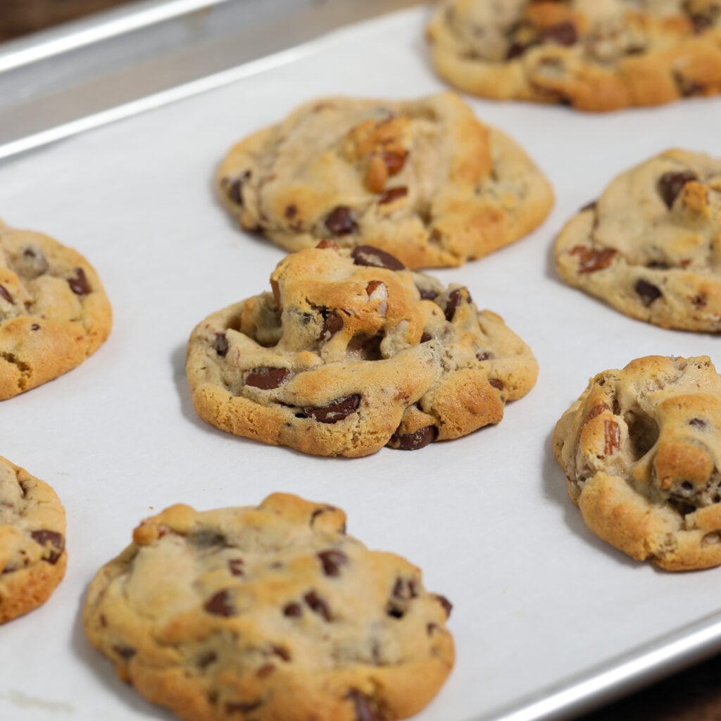 Freshly baked chocolate chip cookies cooling on a parchment-lined baking sheet.flavor and texture.