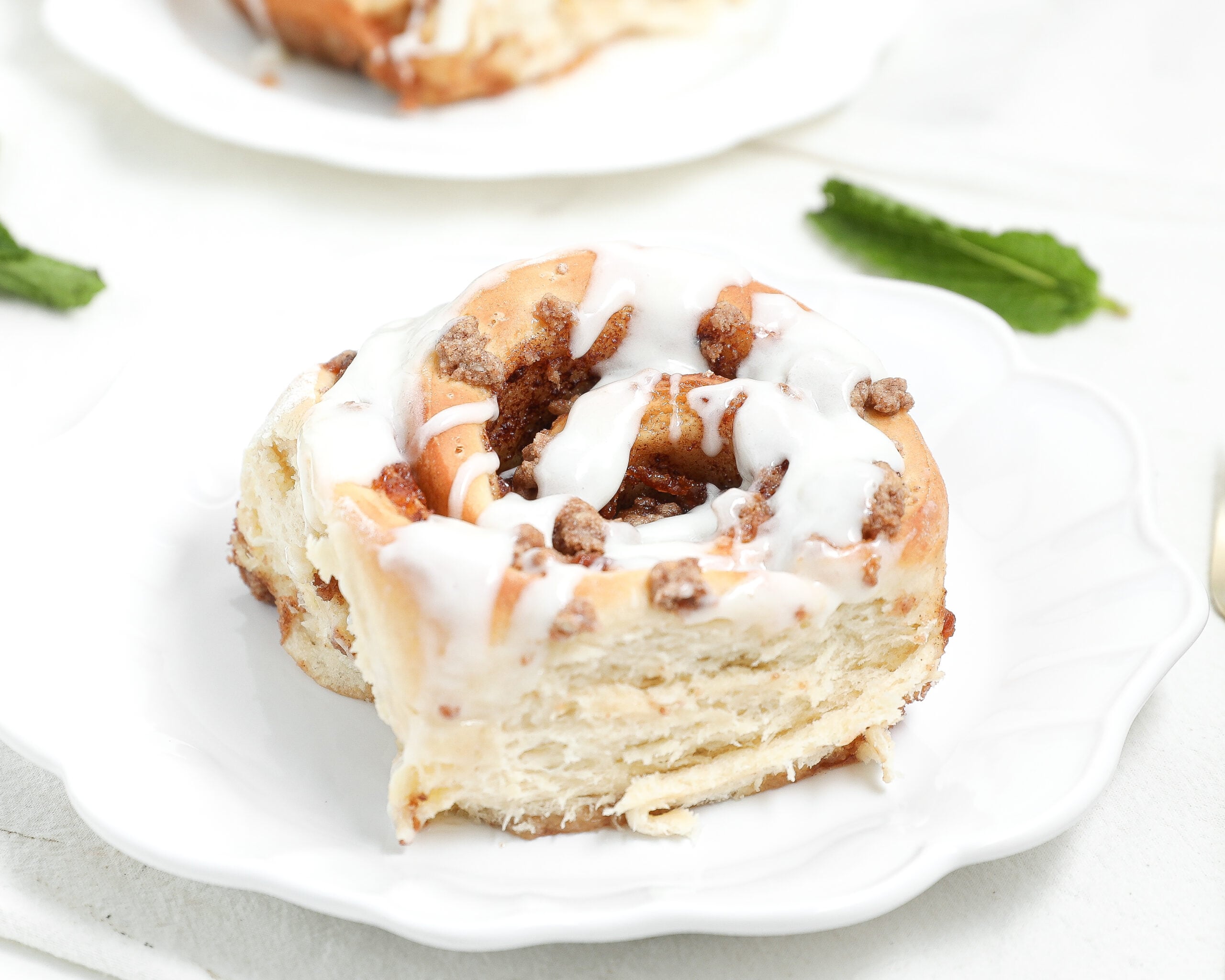 Close-up of a peach cobbler cinnamon roll topped with white glaze on a white plate, showing the soft layered interior and cinnamon-peach filling.