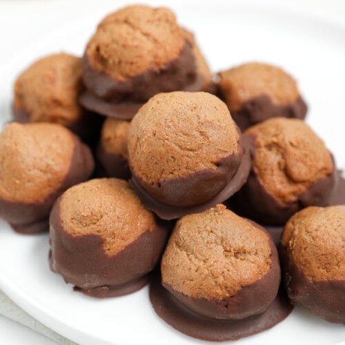 Protein buckeye balls dipped in chocolate and stacked on a white plate.