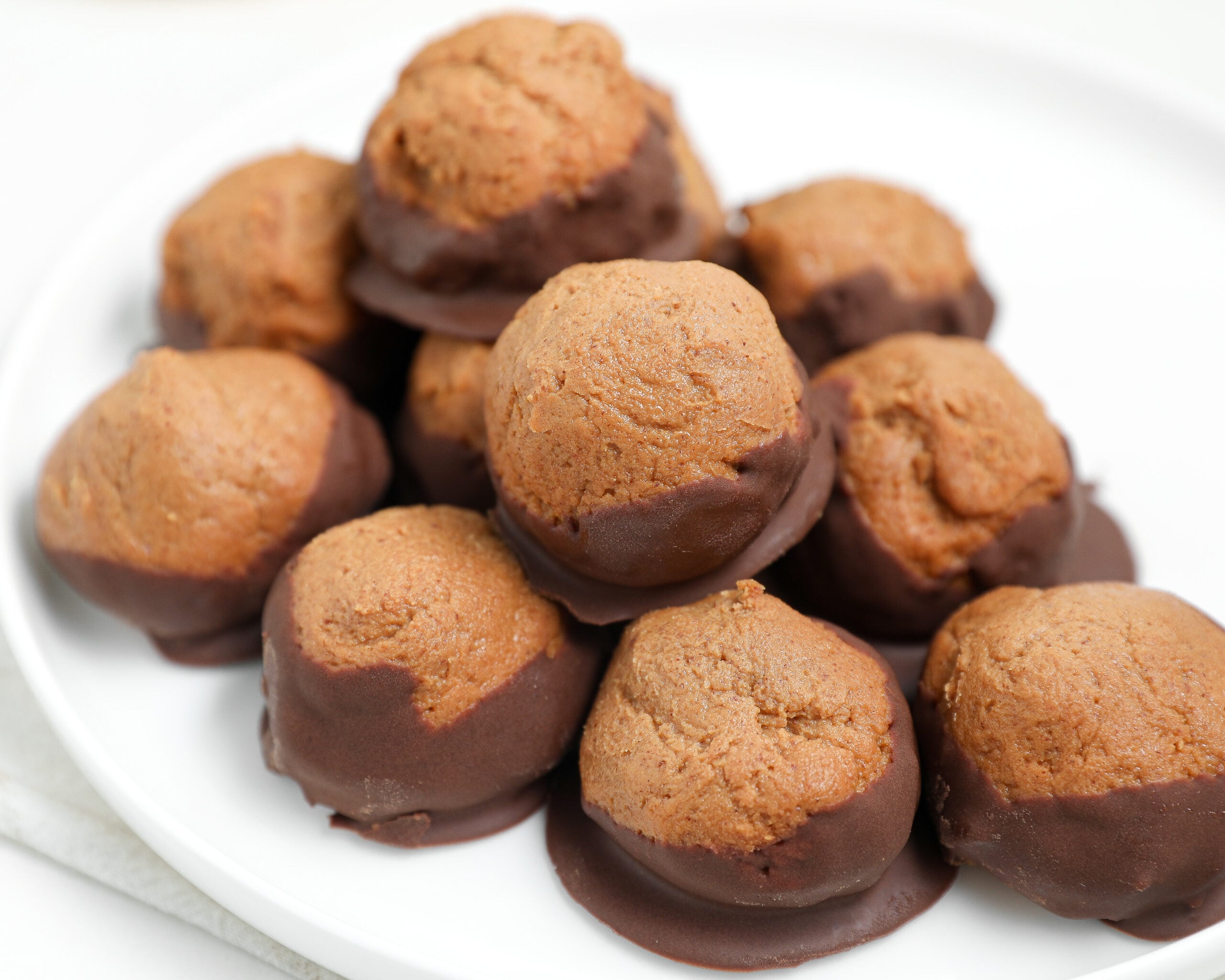 Protein buckeye balls dipped in chocolate and stacked on a white plate.