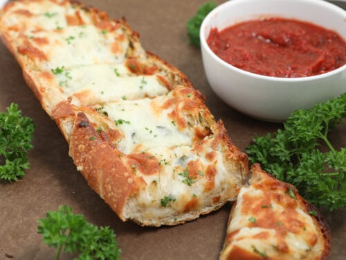 Cheesy garlic bread topped with melted mozzarella and parsley beside marinara sauce