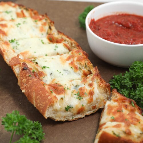 Cheesy garlic bread topped with melted mozzarella and parsley beside marinara sauce