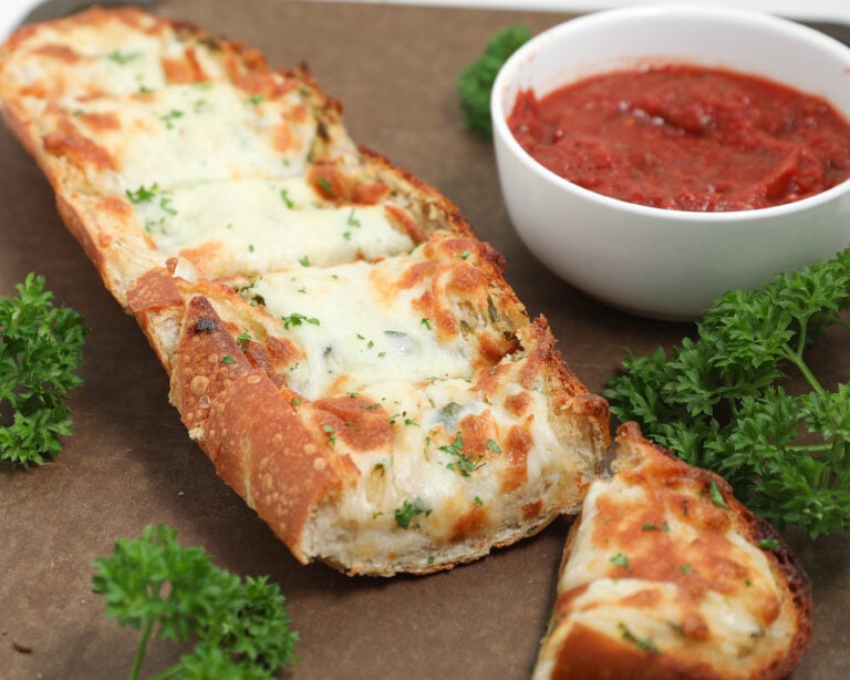 Cheesy garlic bread topped with melted mozzarella and parsley beside marinara sauce