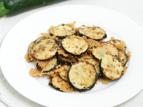 Roasted zucchini slices topped with parmesan cheese on a white plate.