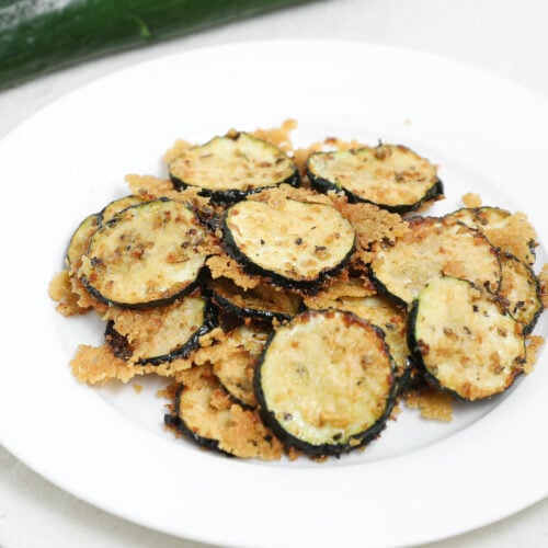 Roasted zucchini slices topped with parmesan cheese on a white plate.