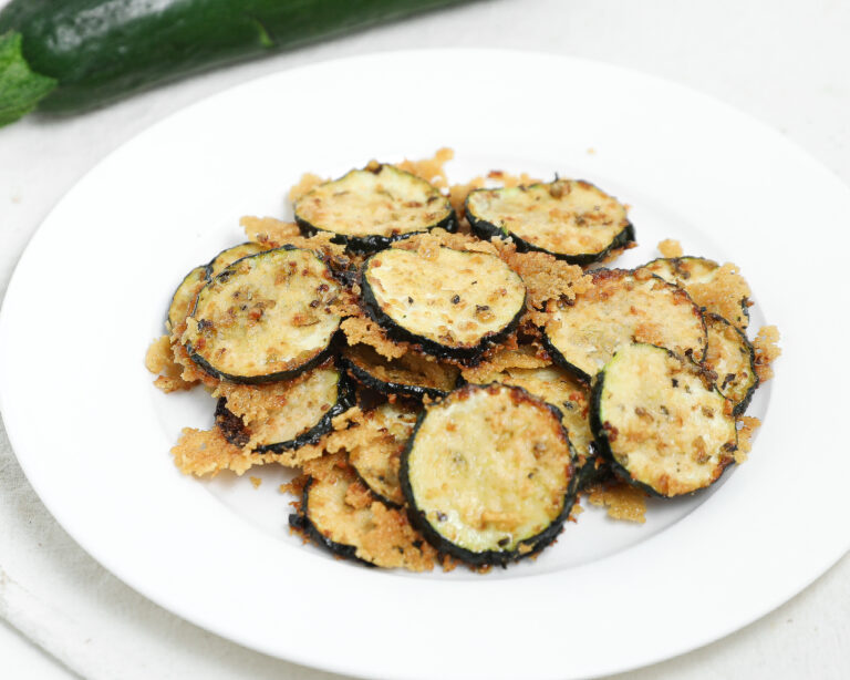 Roasted zucchini slices topped with parmesan cheese on a white plate.
