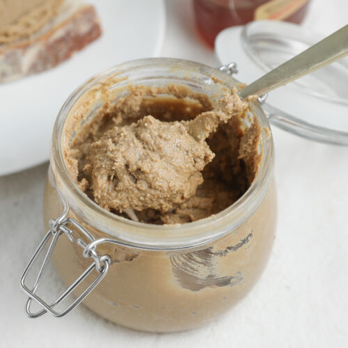Homemade cinnamon honey sunflower seed butter in a glass jar with a spoon.