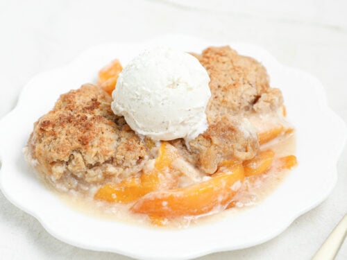 Golden Peach Cheesecake Cobbler baked with layers of sweet peaches, creamy cheesecake filling, and buttery cobbler topping served warm with vanilla ice cream.
