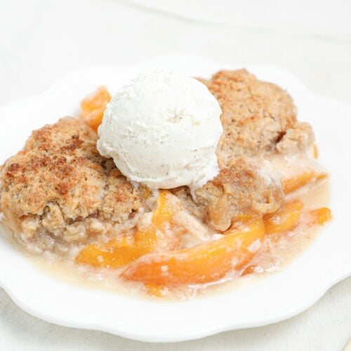 Golden Peach Cheesecake Cobbler baked with layers of sweet peaches, creamy cheesecake filling, and buttery cobbler topping served warm with vanilla ice cream.