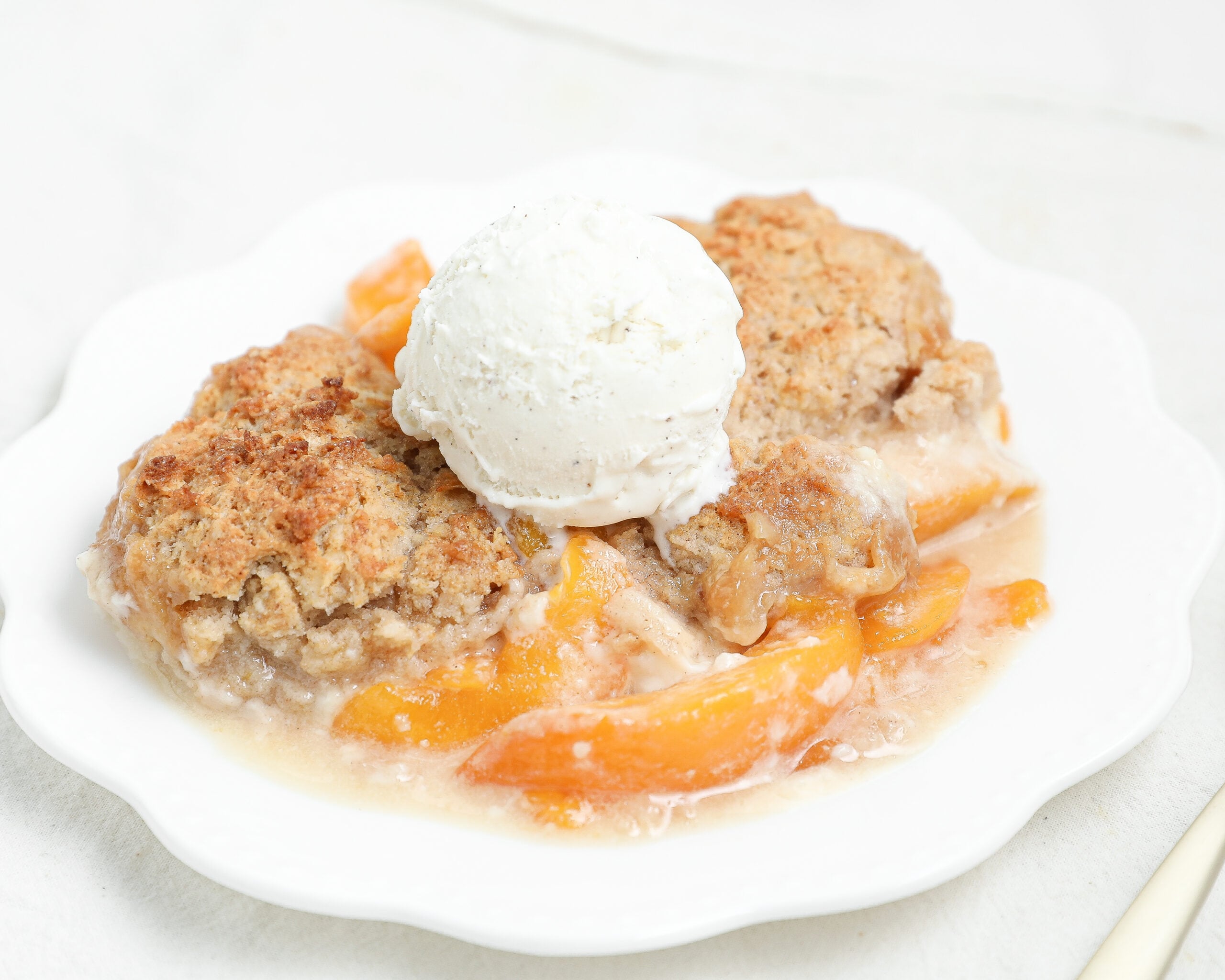 Golden Peach Cheesecake Cobbler baked with layers of sweet peaches, creamy cheesecake filling, and buttery cobbler topping served warm with vanilla ice cream.