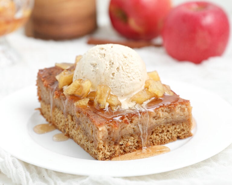 Slice of Caramel Apple Gooey Butter Cake topped with warm cinnamon caramel apples, vanilla ice cream, and caramel sauce on a white plate.