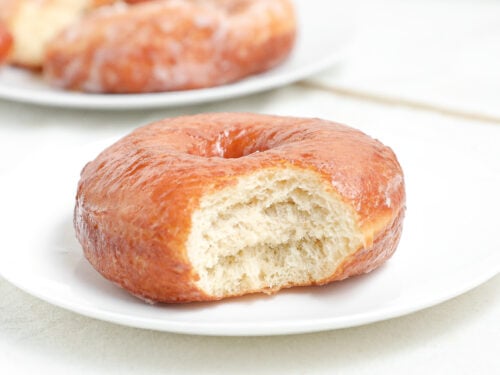 Copycat Krispy Kreme doughnut with vanilla glaze and a bite taken out showing the soft fluffy interior.