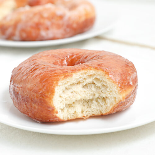 Copycat Krispy Kreme doughnut with vanilla glaze and a bite taken out showing the soft fluffy interior.